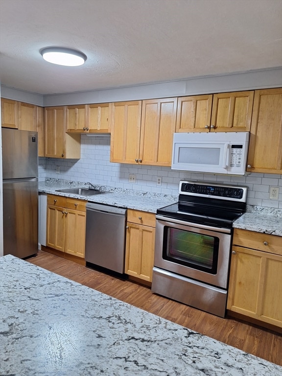 kitchen featuring appliances with stainless steel finishes, tasteful backsplash, sink, and light wood-type flooring