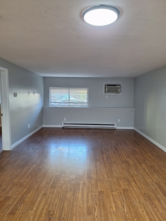 spare room with an AC wall unit, baseboard heating, and hardwood / wood-style floors