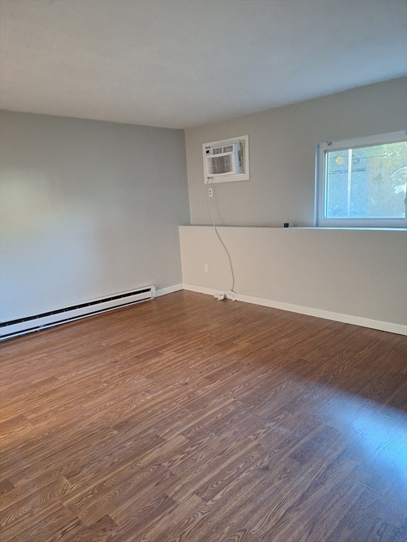 empty room featuring a baseboard radiator, dark hardwood / wood-style flooring, and a wall unit AC