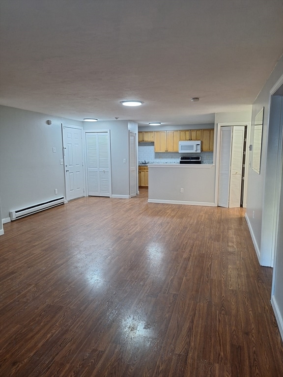 unfurnished living room featuring baseboard heating and dark hardwood / wood-style floors