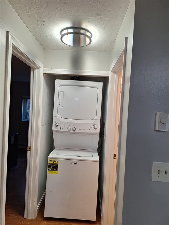 washroom featuring a textured ceiling, stacked washer and dryer, and wood-type flooring