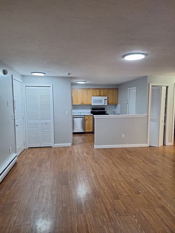 kitchen with a baseboard radiator, appliances with stainless steel finishes, dark hardwood / wood-style flooring, and decorative backsplash