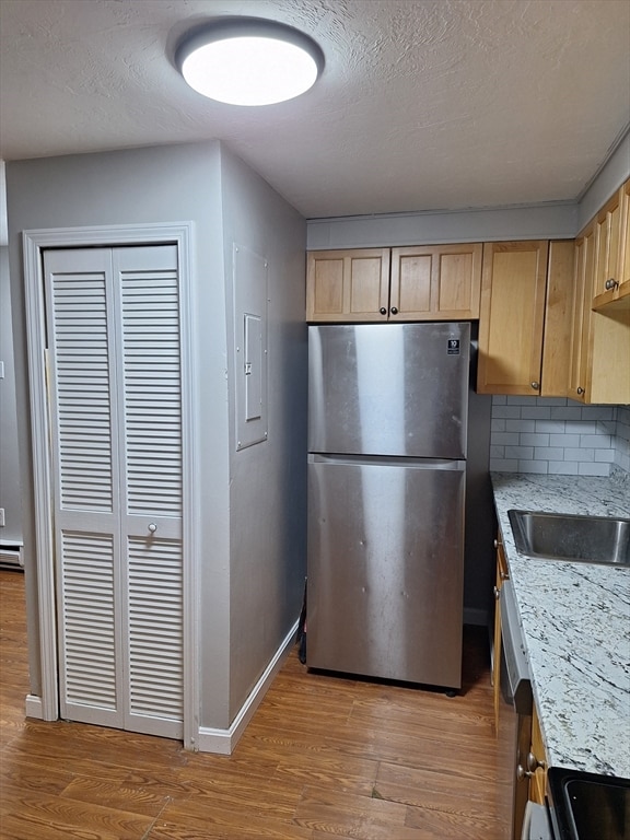 kitchen with stainless steel fridge, backsplash, a textured ceiling, light hardwood / wood-style floors, and light stone counters