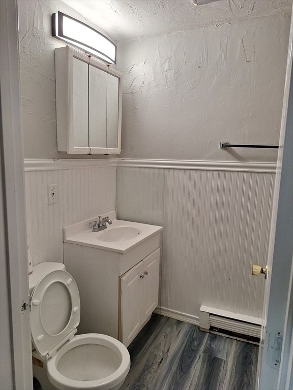 bathroom featuring wood-type flooring, a baseboard heating unit, a textured ceiling, toilet, and vanity