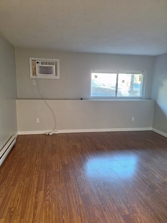 empty room featuring an AC wall unit, a baseboard radiator, and dark hardwood / wood-style flooring