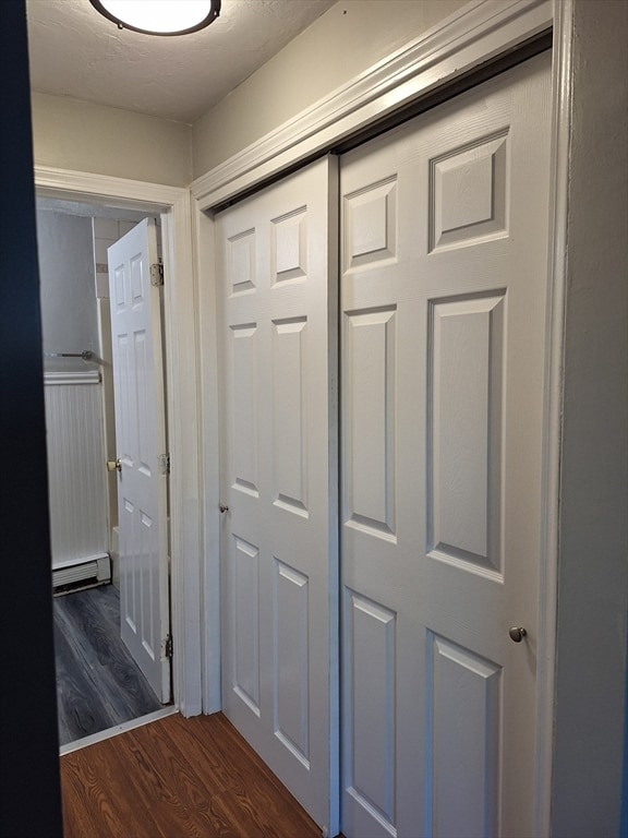 hall with dark wood-type flooring, a textured ceiling, and a baseboard heating unit