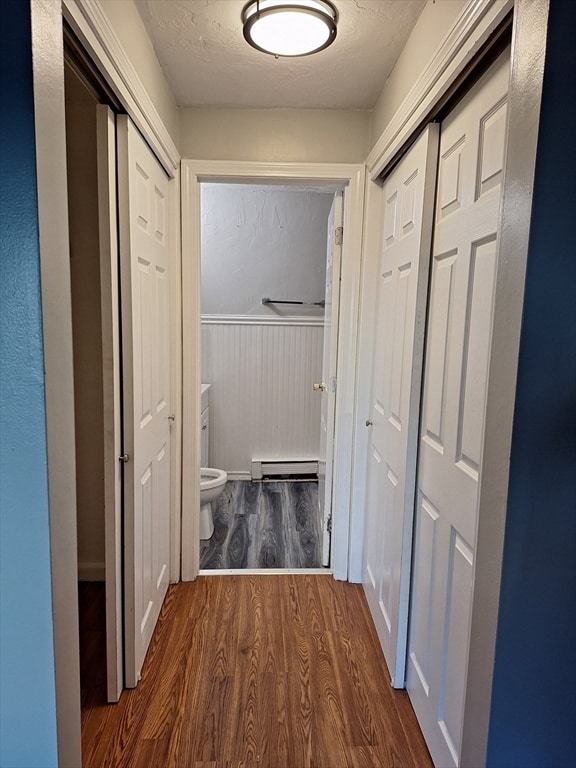 hall featuring dark hardwood / wood-style floors, baseboard heating, and a textured ceiling