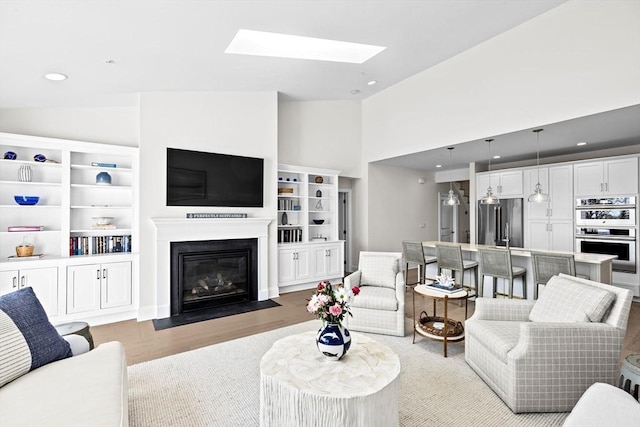 living room featuring light wood-style floors, a fireplace with flush hearth, recessed lighting, and a skylight