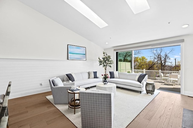 living area featuring baseboards, lofted ceiling with skylight, and wood finished floors