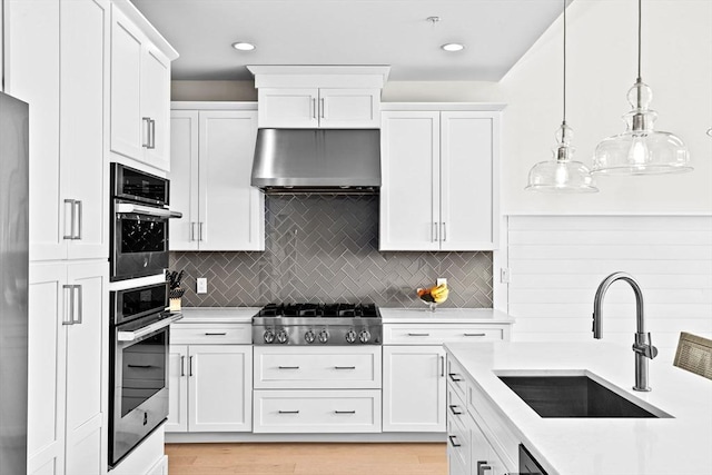 kitchen with light countertops, under cabinet range hood, white cabinets, a sink, and stainless steel gas stovetop