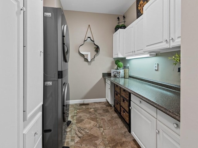 101 Colonial Dr Unit 101, Sturbridge, MA 01566 - laundry room featuring stacked washer / dryer, cabinet space, dark stone finish floors, and baseboards