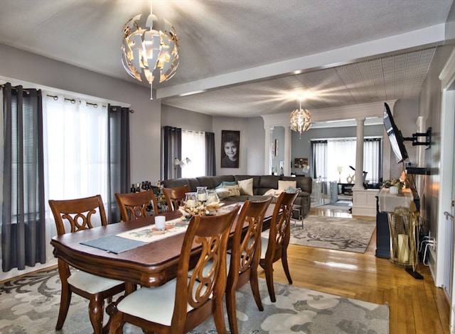 dining area with ornate columns, beam ceiling, an inviting chandelier, a textured ceiling, and light hardwood / wood-style floors