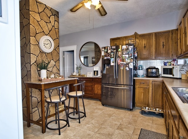 kitchen featuring decorative backsplash, stainless steel refrigerator with ice dispenser, a textured ceiling, and ceiling fan