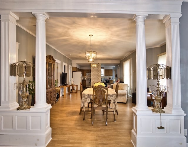 dining room featuring crown molding, light hardwood / wood-style floors, ornate columns, and an inviting chandelier