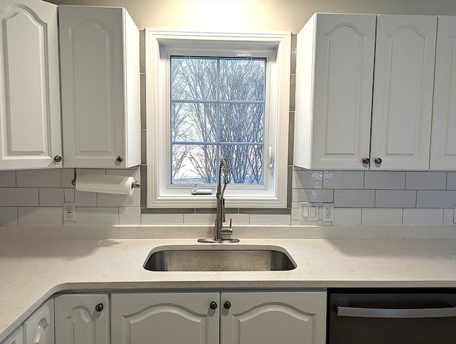 kitchen featuring tasteful backsplash, white cabinetry, a sink, and dishwashing machine