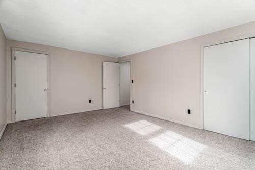 unfurnished bedroom featuring two closets and light carpet