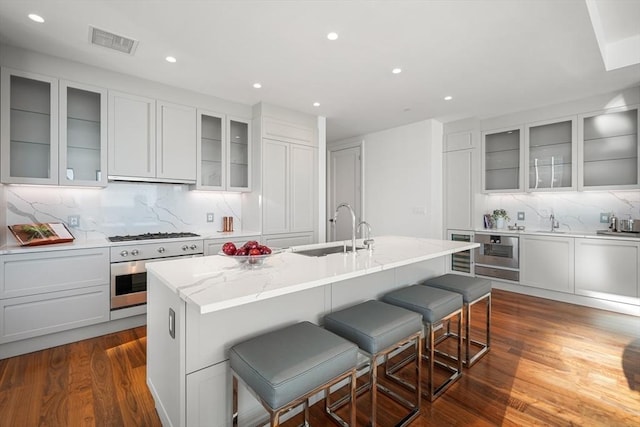 kitchen featuring sink, a breakfast bar area, a center island with sink, dark hardwood / wood-style flooring, and oven