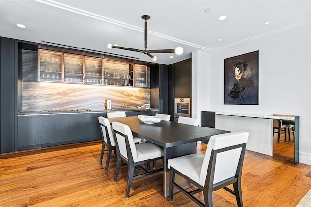 dining area with ornamental molding, light hardwood / wood-style floors, and indoor bar