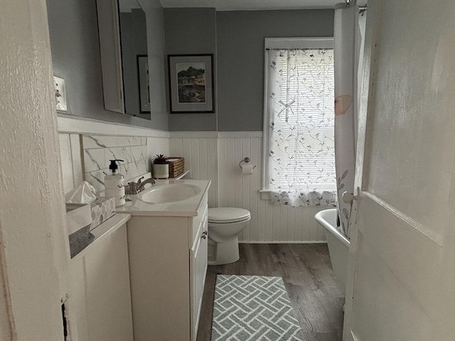bathroom featuring toilet, wainscoting, vanity, a soaking tub, and wood finished floors