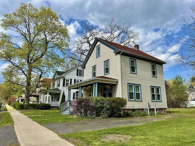 view of side of home with covered porch, a chimney, and a lawn
