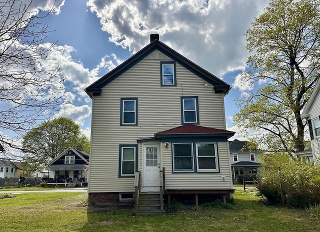 rear view of house with a chimney, entry steps, and a yard
