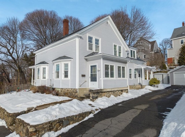 view of front of home featuring driveway, a garage, a chimney, and an outdoor structure