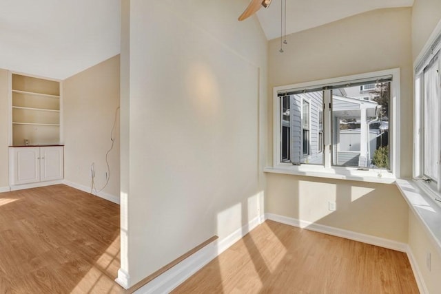 empty room featuring baseboards, built in features, ceiling fan, vaulted ceiling, and light wood-style floors