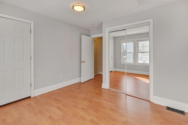 unfurnished bedroom with a closet, wood finished floors, visible vents, and baseboards