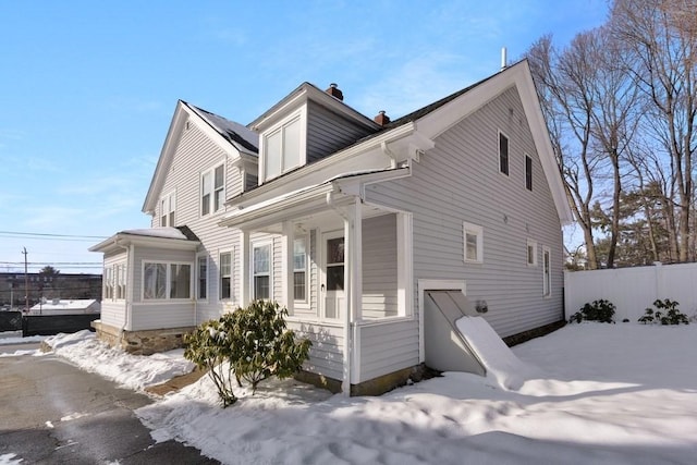 view of snow covered exterior with a chimney and fence