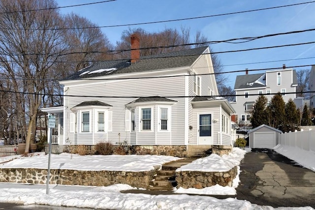 view of front facade featuring aphalt driveway, an outbuilding, a chimney, and a garage