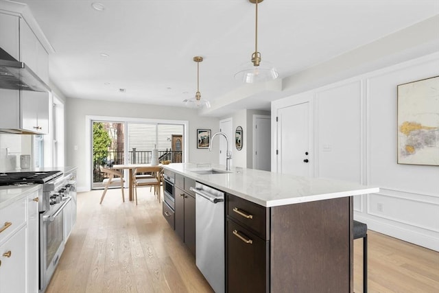 220 Bowen St Unit 2, Boston, MA 02127 - kitchen featuring appliances with stainless steel finishes, a sink, light wood-type flooring, a kitchen island with sink, and white cabinetry