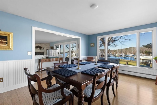 dining space with baseboard heating, wood finished floors, and a wainscoted wall