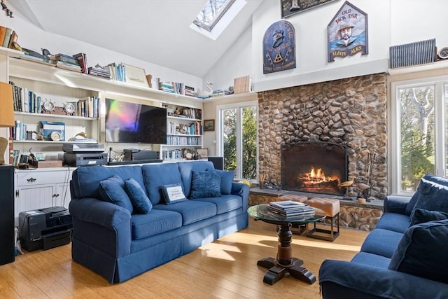 living area with light wood-type flooring, high vaulted ceiling, a skylight, and a fireplace