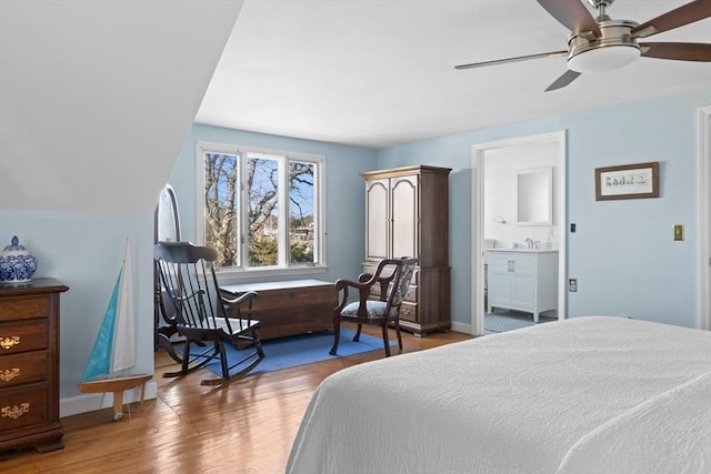 bedroom with vaulted ceiling, connected bathroom, baseboards, and wood finished floors