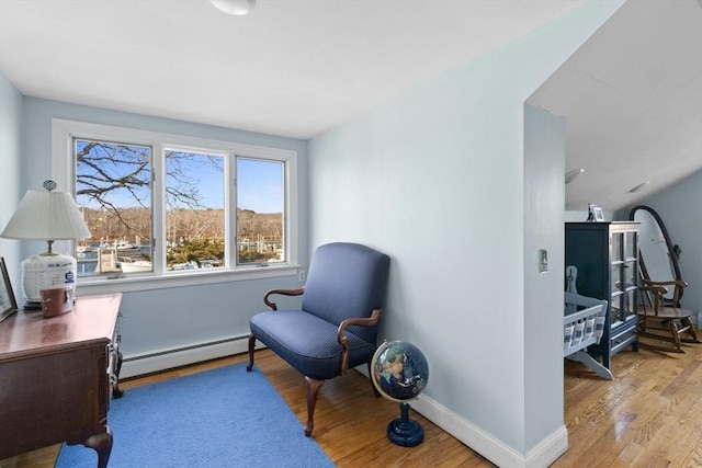 sitting room with a baseboard heating unit, baseboards, and light wood-style flooring