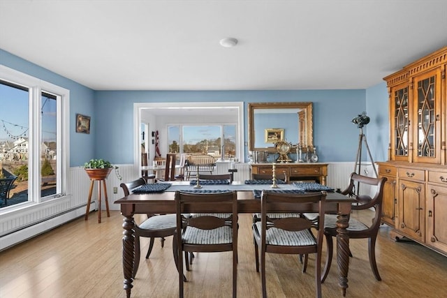 dining room with light wood finished floors, a wainscoted wall, and a baseboard radiator