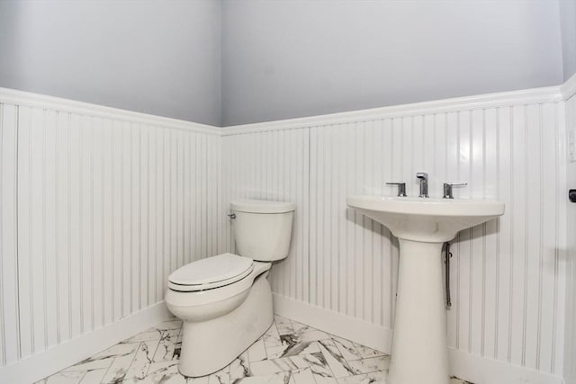 half bath with a wainscoted wall, marble finish floor, and toilet