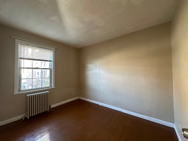 empty room with dark wood-type flooring and radiator heating unit