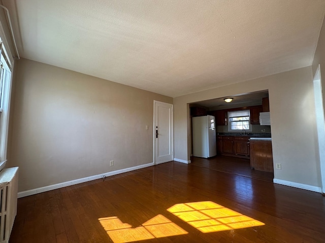 unfurnished living room featuring dark wood-type flooring, radiator, sink, and a textured ceiling