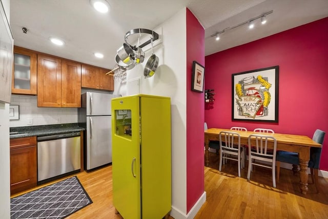 kitchen featuring brown cabinets, dark countertops, stainless steel appliances, light wood-type flooring, and tasteful backsplash