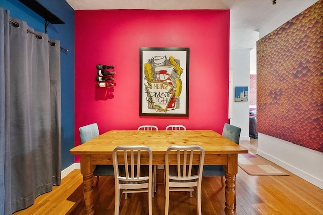 dining area featuring baseboards, an accent wall, and wood finished floors