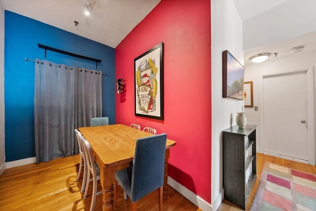 dining room featuring rail lighting, baseboards, and light wood finished floors
