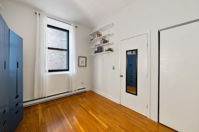 unfurnished bedroom featuring a baseboard heating unit and wood finished floors