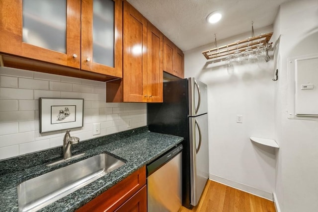 kitchen with decorative backsplash, brown cabinets, dishwasher, a sink, and light wood-style floors