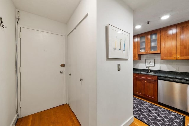 kitchen with stainless steel dishwasher, wood finished floors, dark countertops, glass insert cabinets, and brown cabinets