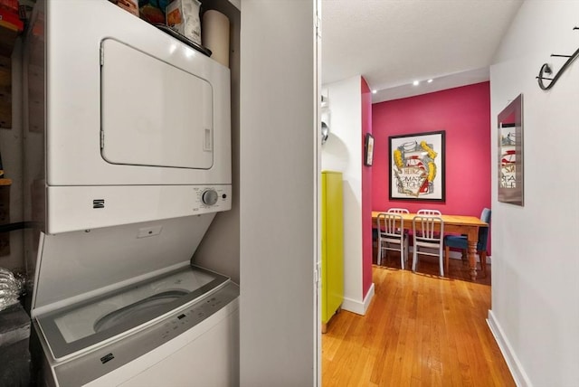 laundry area featuring stacked washer and dryer, baseboards, light wood-style flooring, and laundry area