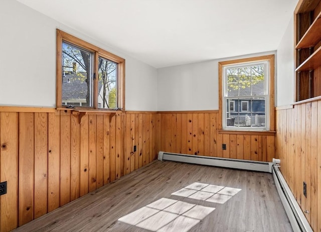 empty room with wood walls, a baseboard radiator, wood finished floors, and a wainscoted wall