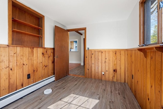 spare room with wainscoting, wood finished floors, a baseboard heating unit, and wood walls