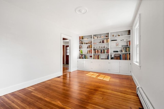 empty room with a baseboard radiator, light wood finished floors, and baseboards