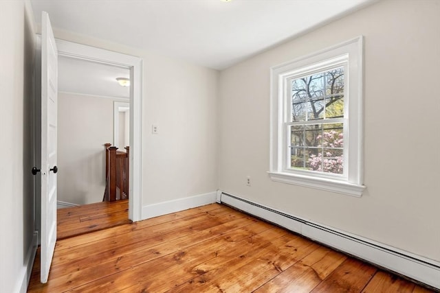 unfurnished room with a baseboard radiator, light wood finished floors, and baseboards